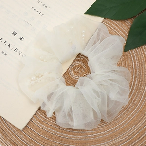 Creamy organza scrunchie with embedded pearls on a woven mat for hair styling