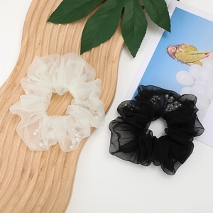 Detail view of mesh scrunchies featuring decorative pearls in white and black fabric