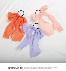 Detailed view of three chiffon bow hair ties in bright orange, lavender, and soft pink shades