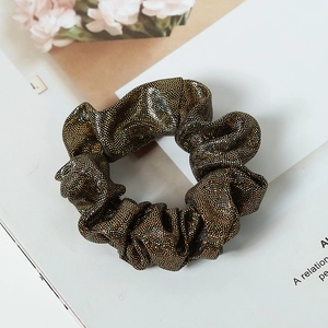 Macro detail of sparkly gold sequin fabric hair scrunchie on a decorative background
