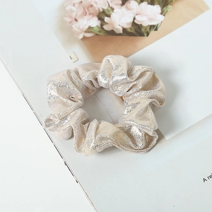 Detail of elegant gold sequined fabric scrunchie with soft pleats on decorative background