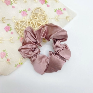 Détail macro du chouchou en satin de soie rose poudré avec texture plissée et éclat