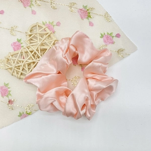 Vue détaillée du chouchou en satin de soie rose tendre sur un tissu floral décoratif