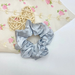 Détail du chouchou en satin bleu clair sur un tissu blanc brodé de fleurs