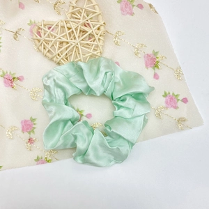 Texture détaillée de chouchou en satin de soie vert menthe sur fond de tissu floral