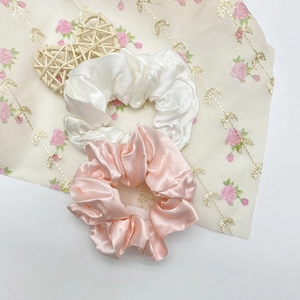 Détail des chouchous en satin de soie blanc perle et rose sur un fond en tissu floral