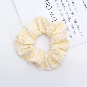 Close-up of light yellow floral jacquard fabric hair scrunchie on a white aesthetic background