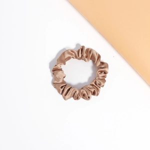 Macro detail of champagne satin hair scrunchie showing glossy silk texture and elegant folds