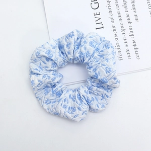 Light blue floral scrunchie with pleated texture shown on a minimalist white backdrop