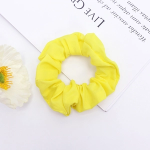 Chouchou en tissu jaune vif minimaliste avec des plis doux sur un fond blanc épuré