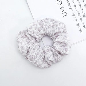 Close-up of white floral scrunchie with purple flower patterns and pleated fabric detail