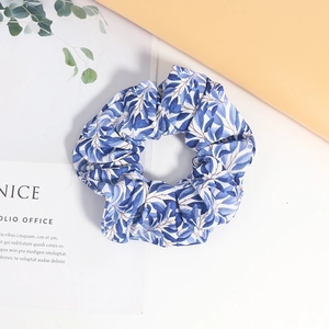 Détail d'un chouchou en tissu avec motif de feuilles bleues sur texture fond blanc