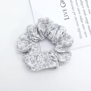 Close-up of a grey floral fabric scrunchie with soft pleated texture on white background