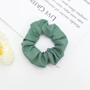Détail d'un chouchou en tissu vert sur fond blanc avec des fleurs séchées