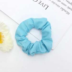 Détail d'un chouchou en tissu bleu ciel avec plis délicats sur un fond de style épuré