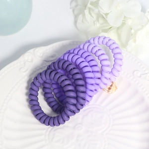 Close-up of matte purple spiral hair ties arranged neatly on a decorative white porcelain tray
