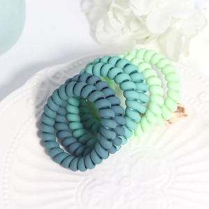 Close-up of four matte green gradient spiral hair ties displayed on a ceramic dish