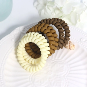 Close-up of four matte telephone wire hair ties in earthy tones on a white ceramic dish