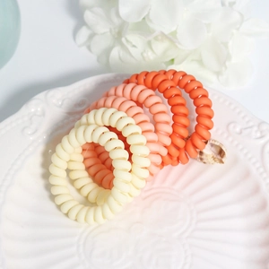 Close-up of five matte colorful spiral telephone wire hair ties on a white ceramic plate