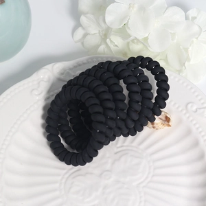 Set of five matte black spiral hair coils displayed on an elegant ceramic tray