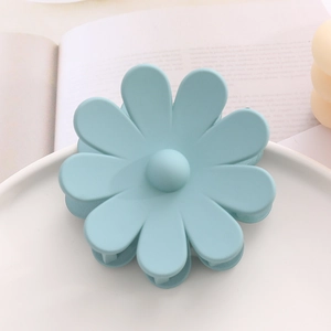 Détail d'une pince à cheveux marguerite bleu clair mat sur un plateau en céramique