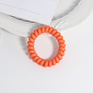 Detailansicht eines matten orangefarbenen Spiralhaargummis auf einem weißen Zierteller
