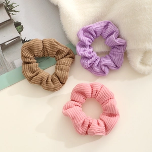 Three knitted waffle texture scrunchies in brown, lavender, and pink in a lifestyle setting