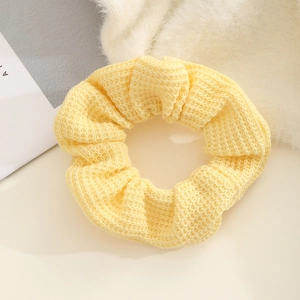 Close-up of light yellow knitted scrunchie showing detailed hollow weave texture and fabric
