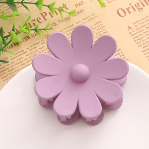 Détail d'une pince à cheveux en forme de fleur violette mate sur un plat décoratif blanc