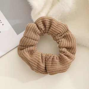 Close-up detail of a brown knitted scrunchie showing fine ribbed wool texture on white plush