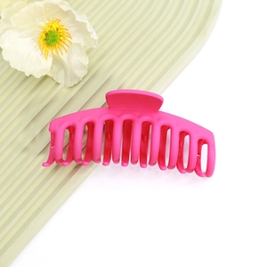 Gros plan d'une grande pince à cheveux rose rouge mate avec design à dents sur fond vert