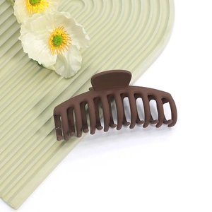 Gros plan d'une grande pince à cheveux marron mat avec dents imbriquées sur fond vert