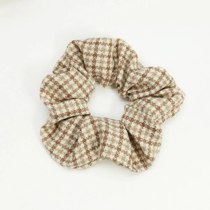 Detailed close-up of brown houndstooth fabric scrunchie hair tie on white background