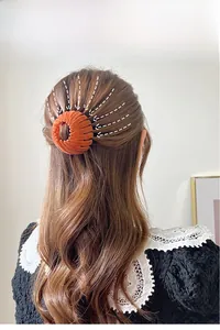 Detail showing an orange-red velvet bird nest hair ring on a woman's hair in a bun