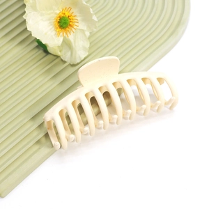 Macro d'une pince à cheveux mate beige avec ressort métallique sur un support vert ondulé
