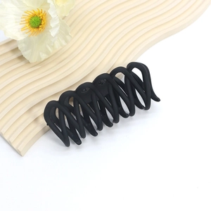 Close-up of a matte black wavy hair claw clip displayed on a minimalist beige wave plate