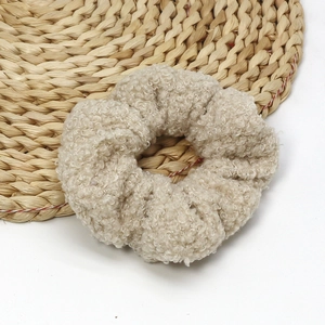 Oatmeal beige fluffy faux shearling scrunchie hair tie on a woven straw mat