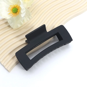 Matte black rectangular hair claw clip with geometric cutout on a beige textured display