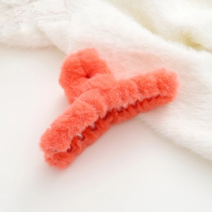 Dettaglio della molletta per capelli in peluche corallo con texture morbida su pelliccia bianca