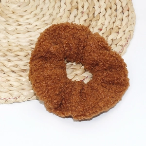 Detailed view of brown plush lamb velvet hair scrunchie on a woven straw mat
