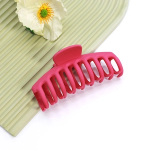 Gros plan sur la pince à cheveux rose mat avec design multi-dents sur fond vert