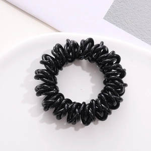 Macro detail of high-elastic black spiral telephone wire hair tie on white plate