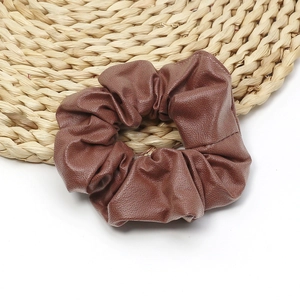 Elegant dark brown PU leather scrunchie with soft texture on a natural woven mat