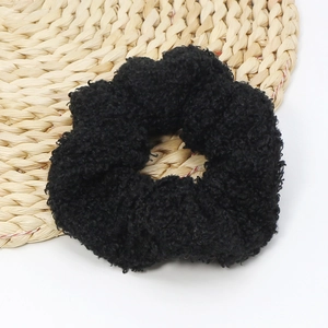 Close-up of black fuzzy lamb wool scrunchie with soft plush texture on a woven mat