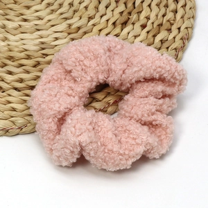 Detail of pink faux shearling scrunchie hair tie on a rustic woven mat accessory
