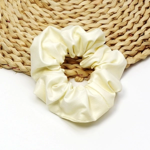 Creamy beige faux leather scrunchie with soft pearl finish on woven background