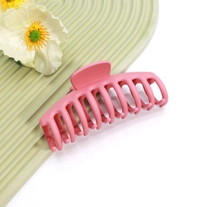 Détail de la grande pince à cheveux rose mat avec dents entrelacées sur fond rayé vert