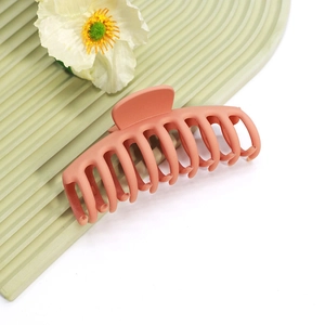 Gros plan d'une pince à cheveux mate rouge brique sur un support ondulé minimaliste