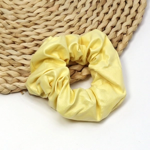 Detailed view of yellow PU leather scrunchie with soft texture on a woven straw mat