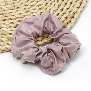 Close-up of elegant faux leather scrunchie in dusty rose on a woven texture mat